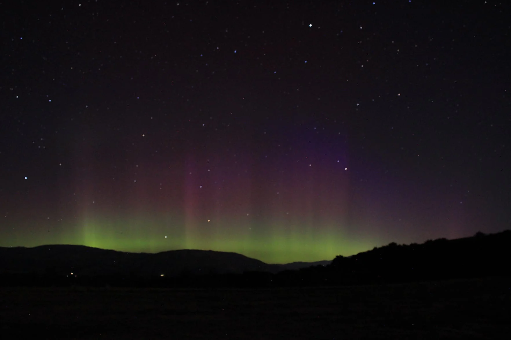 Green and purple Aurora Australis glowing over the hills