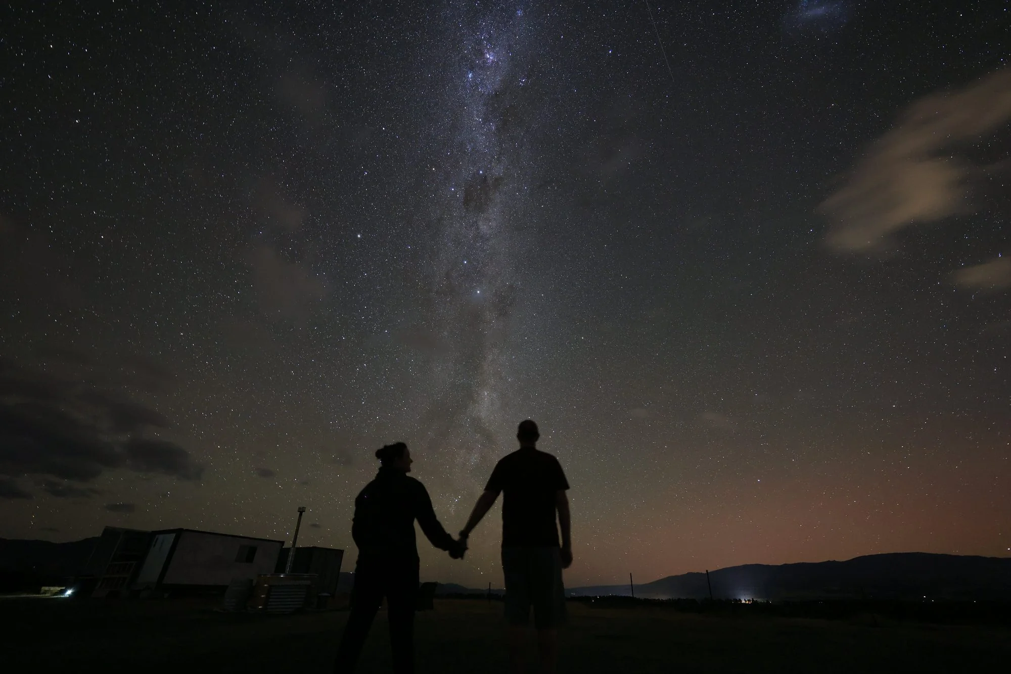 Two people holding hands beneath the Milky Way on the farm